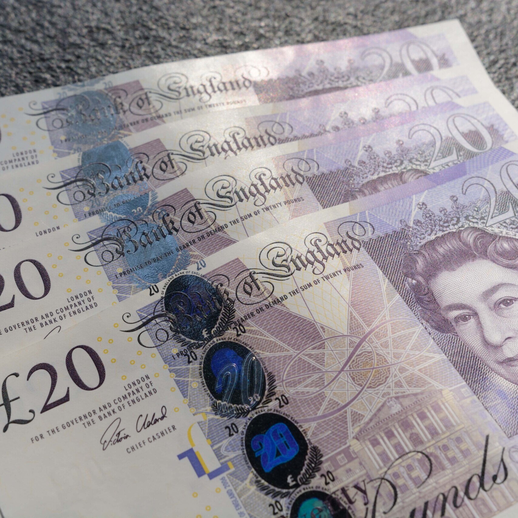 Closeup shot of four twenty-pound sterling bills on a gray background